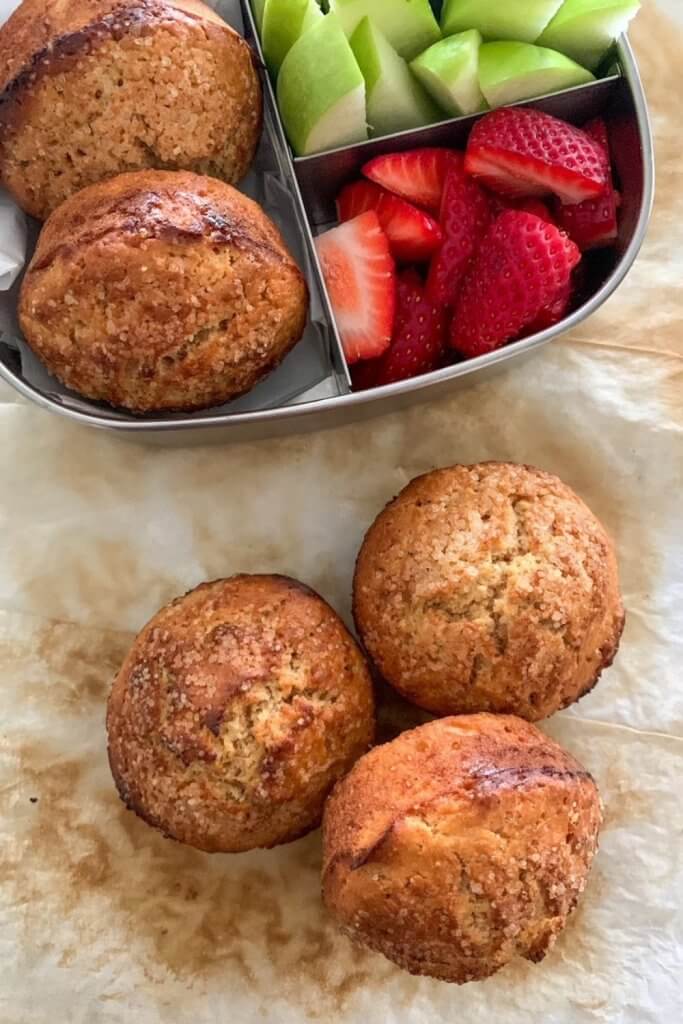 Sourdough cinnamon muffins in a stainless steel lunchbox with strawberries and apple.