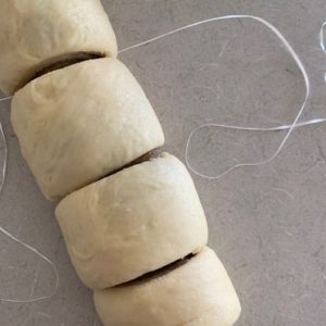 Dough is rolled up with filling inside. Using dental floss to cut each roll with precision.