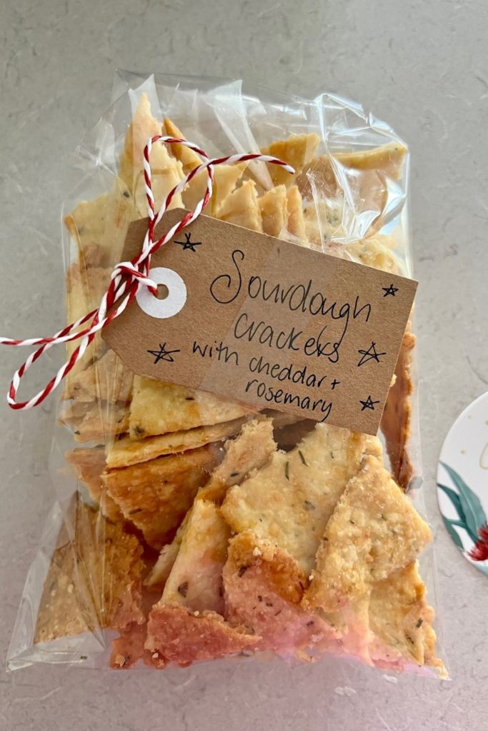 Sourdough discard crackers wrapped in a cellophane bag, tied with red and white twine and labelled with a brown kraft handwritten label.