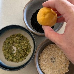 dipping each sourdough pumpkin dinner roll into seeds