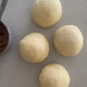 4 balls of dough with a bowl of nutella sitting to the side.