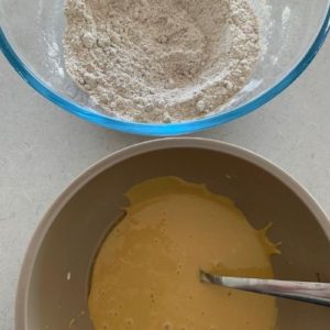 a glass bowl containing all the dry ingredients and a plastic bowl containing all the wet ingredients whisked together.