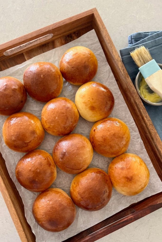 Sourdough brioche buns displayed on a tray next to a pastry brush.