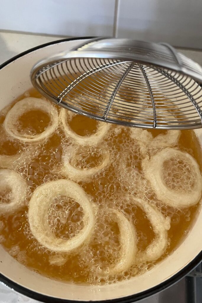 sourdough onion rings floating in hot oil. They are still a little pale and need to cook a bit longer.