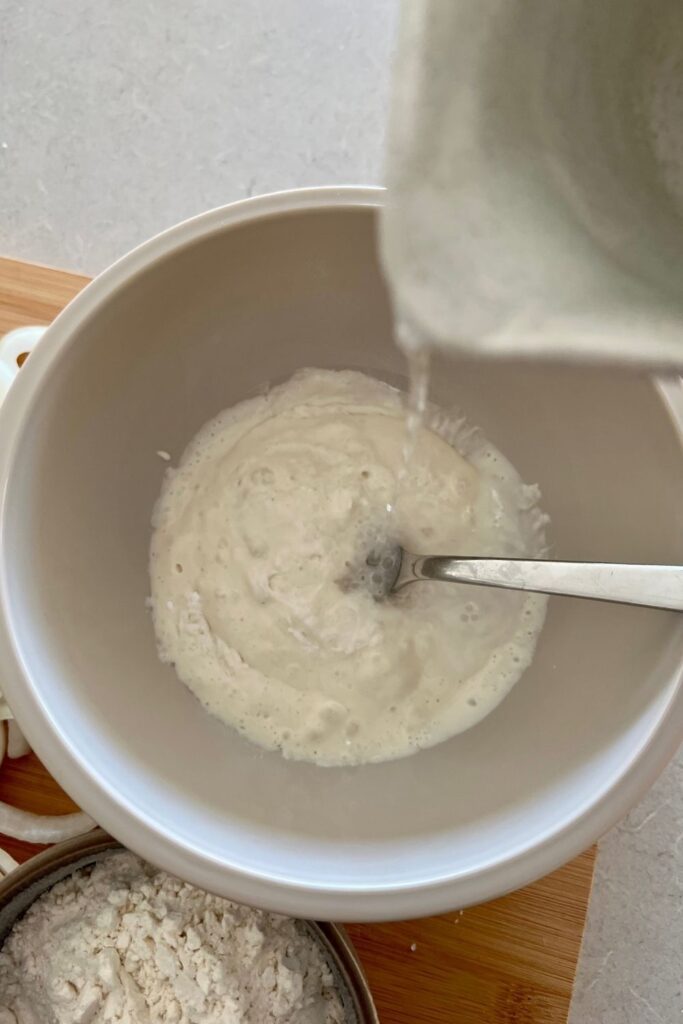 Sourdough starter in a bowl with a fork. Soda water is being poured into the bowl from above to create the sourdough batter.