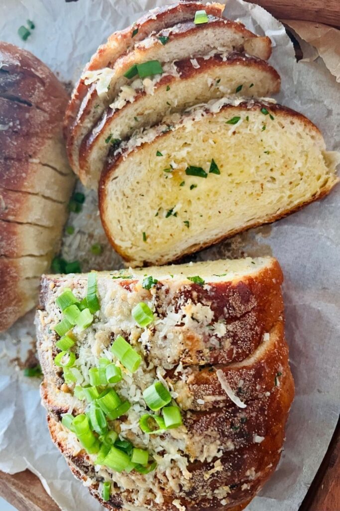 Sourdough garlic bread topped with parmesan and chives. There is piece laying open so you can see the melted butter and parsley inside.