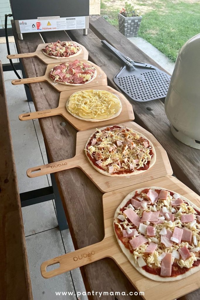 Homemade pizzas lined up on a wooden table.
