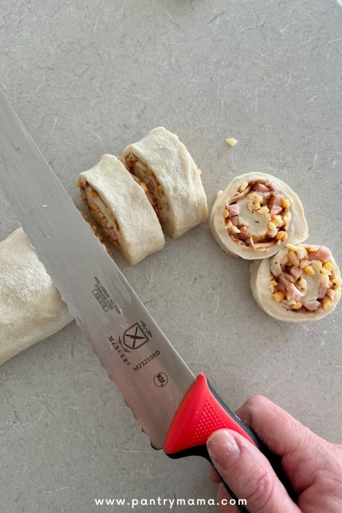 Using a bread knife to measure and cut the pizza rolls to size.