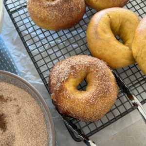 Sourdough Pumpkin Bagels being dipped in butter and cinnamon sugar