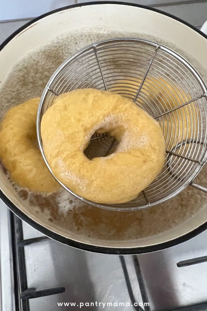 Boiling sourdough pumpkin bagels in honey water and using a slotted spoon to remove them from the boiling water.