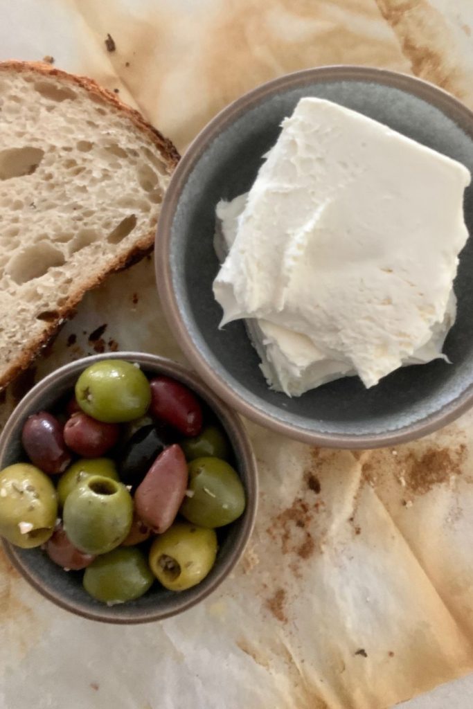 Bowl of mixed olives sitting next to a block of cream cheese.