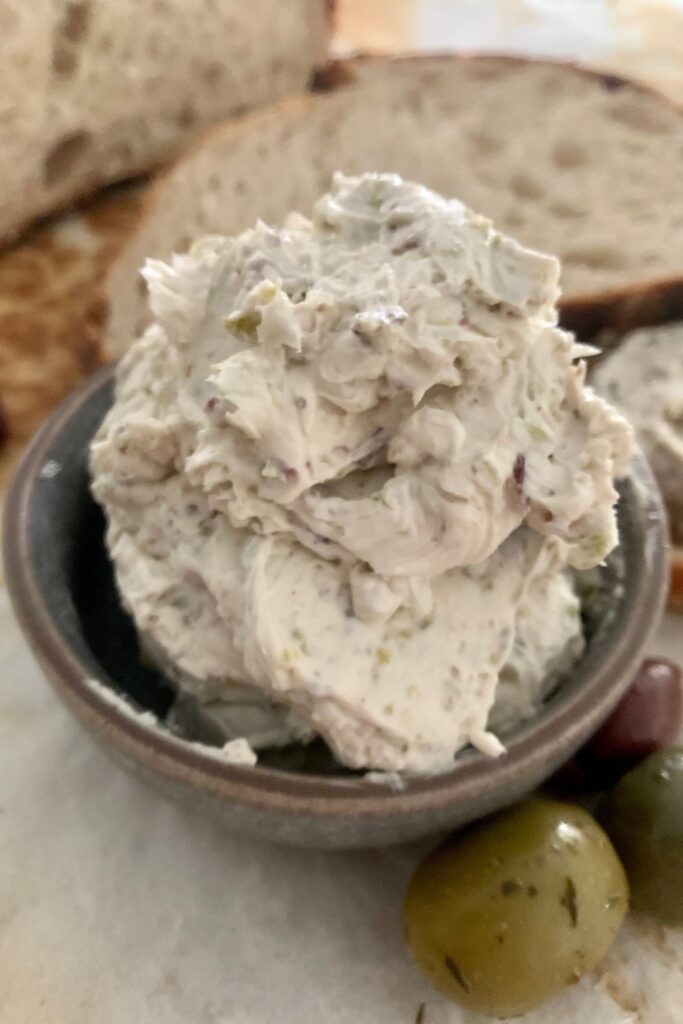 Bowl of olive cream cheese spread sitting in front of sourdough bread.