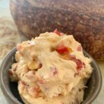 Roasted Red Pepper Cream Cheese Dip or Spread sitting in a bowl in front of a loaf of sourdough bread.