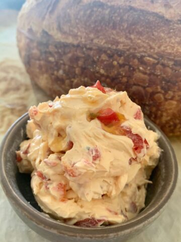 Roasted Red Pepper Cream Cheese Dip or Spread sitting in a bowl in front of a loaf of sourdough bread.