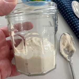 yogurt sourdough starter in a jar with a mixing spoon sitting next to the jar