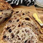 Walnut Raisin Sourdough Bread that has been sliced and arranged so you can see the "bunny" in the bread. There is a black and white dish towel sitting in the background and a wooden butter knife to the right of the sliced sourdough bread.