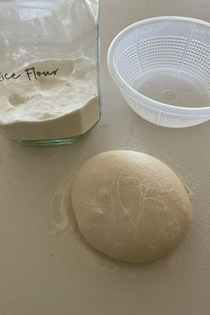 Jar of rice flour sitting next to a ricotta basket (banneton for sourdough) and a sourdough boule coated in rice flour.