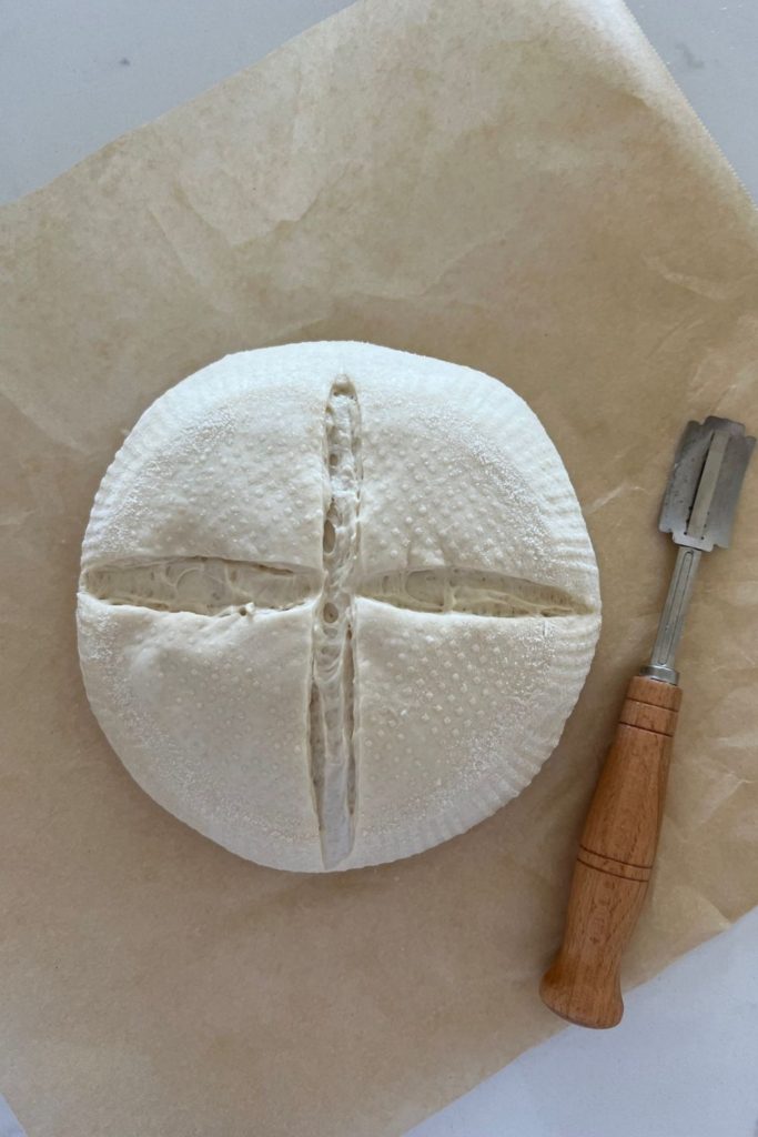Sourdough that has been scored with a cross using a wooden handled lame.