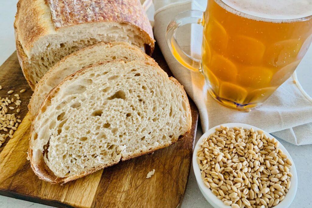 Sourdough beer bread made using flour, beer and salt. There is a loaf of sourdough beer bread that has been sliced and a mug of beer sitting to the right of the photo.