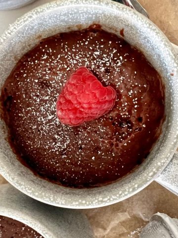Sourdough discard mug cake served in a stoneware mug. The photo is taken above the mug so you can see the top of the mug cake with a fresh red raspberry on top.