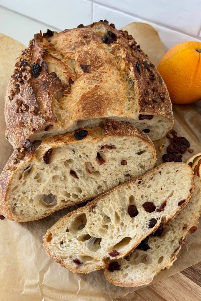 A loaf of orange cranberry sourdough bread that has had 3 slices cut off it. There is an orange in the background.