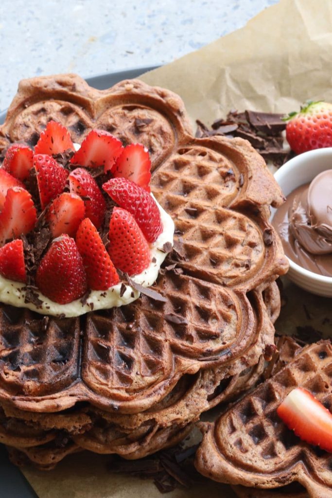 Close up photo of a stack of sourdough chocolate waffles topped with whipped cream and strawberries.